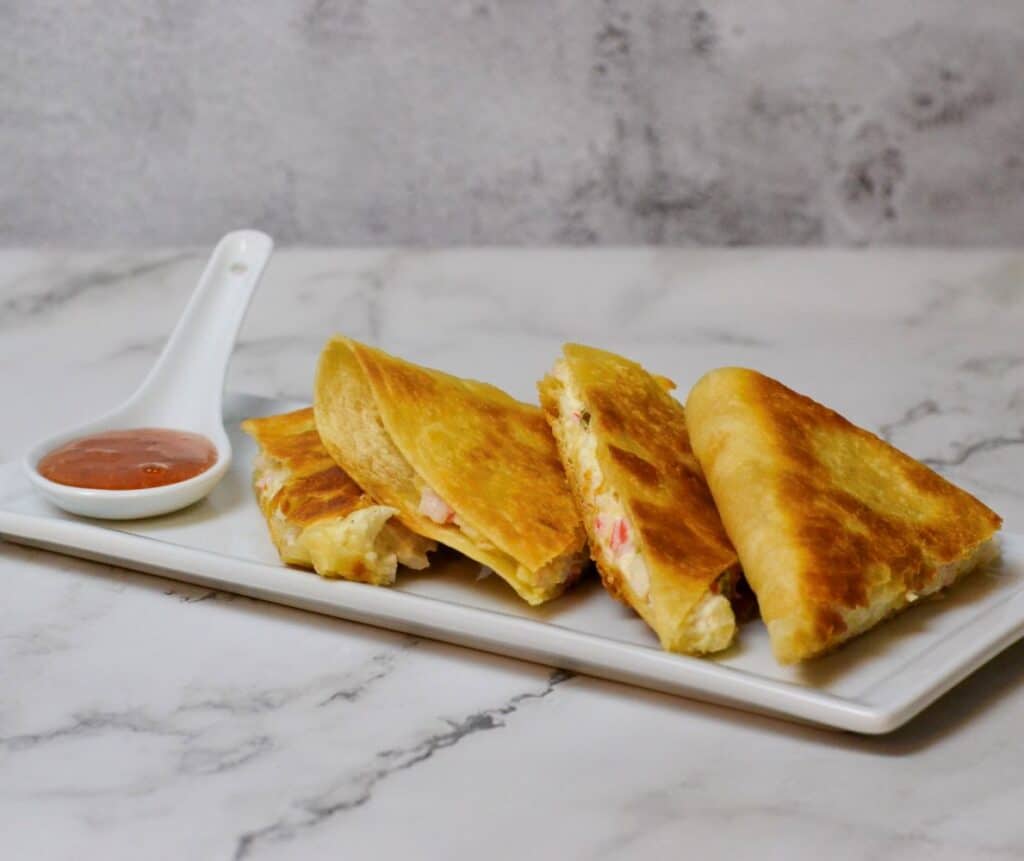 Crab Rangoon Quesadilla cut into wedges on white plate with plum dipping sauce