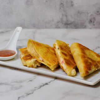 Crab Rangoon Quesadilla cut into wedges on white plate with plum dipping sauce