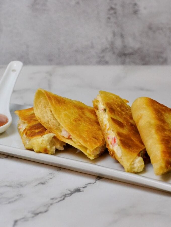 Crab Rangoon Quesadilla cut into wedges on white plate with plum dipping sauce